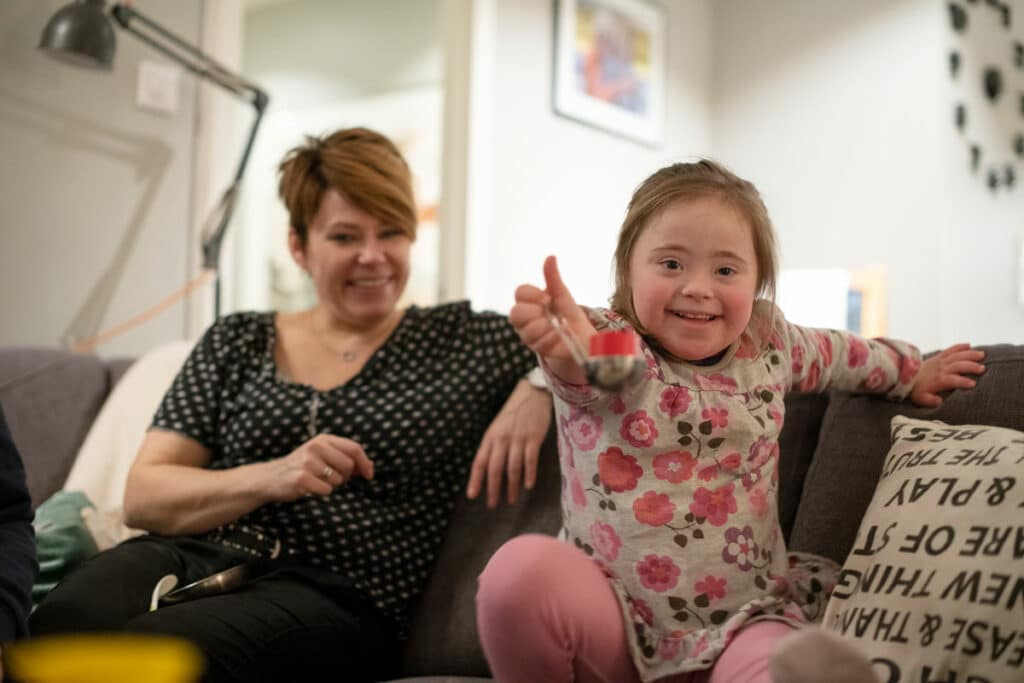 Liten jente  med Downs syndrom viser frem gele på skje til fotografen. Stella sammen med mamma Lene Lindquist