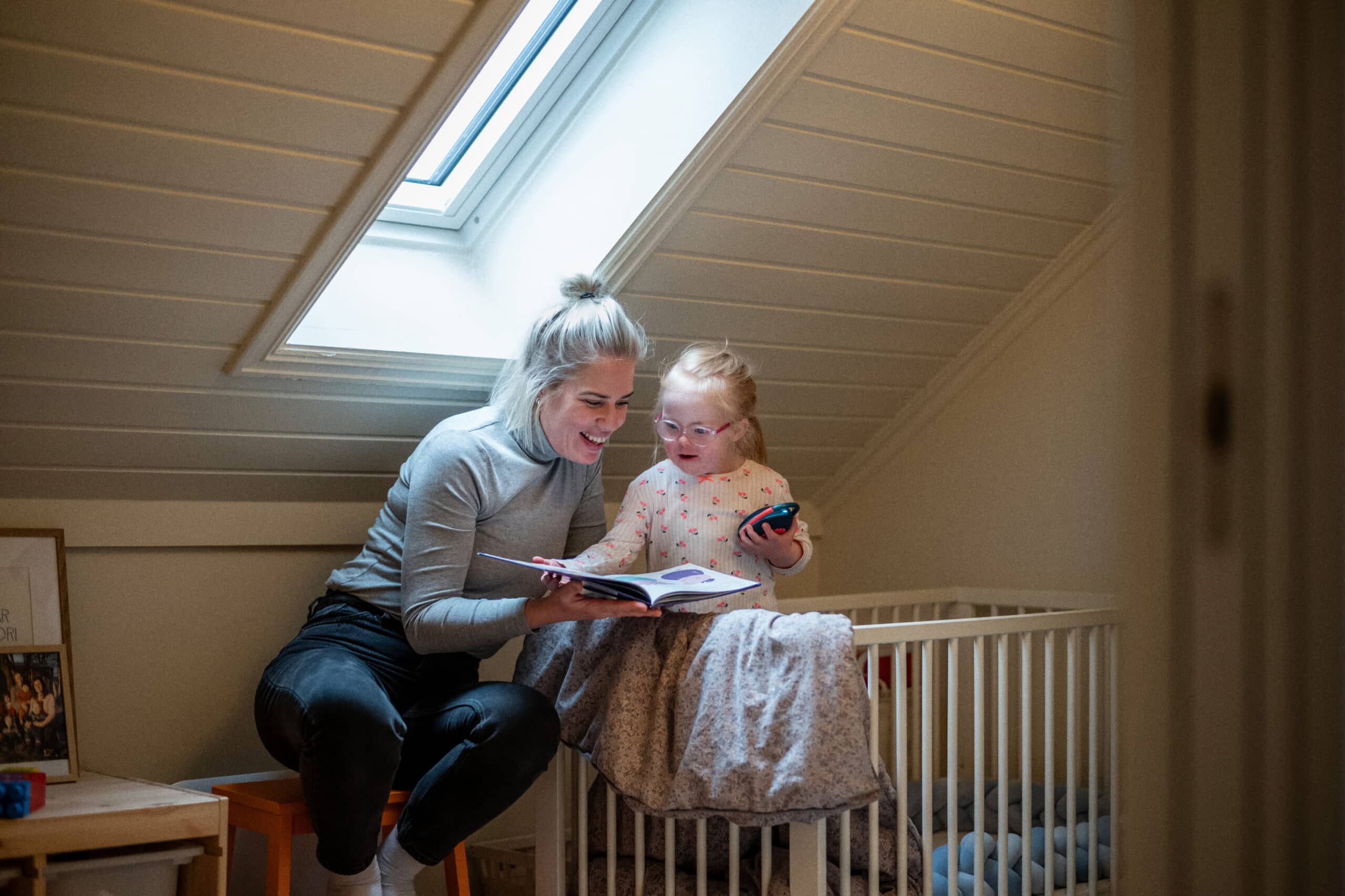 Mor og datter med Downs syndrom leser bok sammen på sengekanten